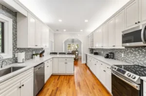 A kitchen with white cabinets and wood floors.