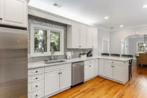 A kitchen with white cabinets and wood floors.
