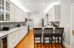 A kitchen with white cabinets and black chairs.