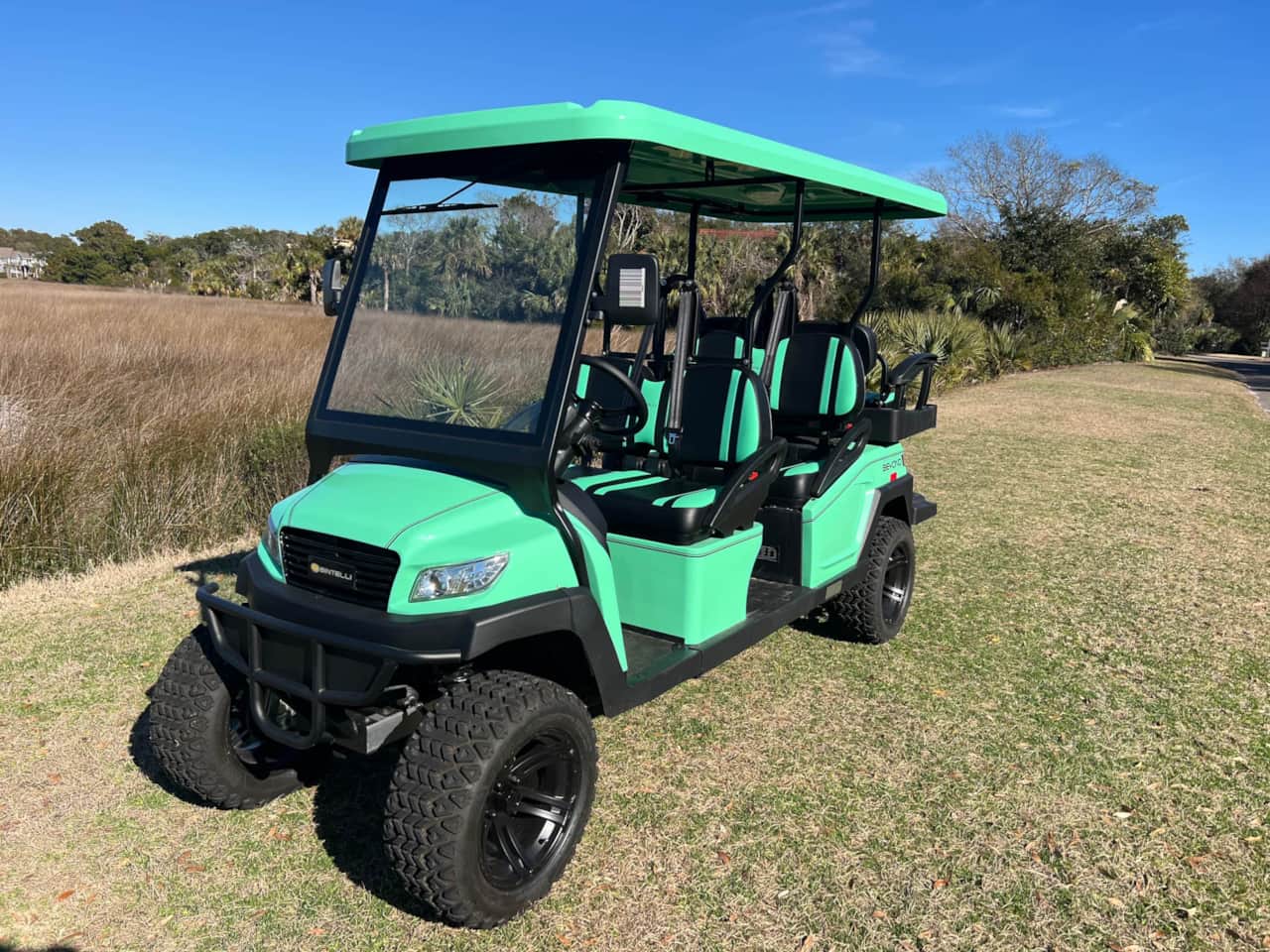 A green golf cart is parked in the grass.
