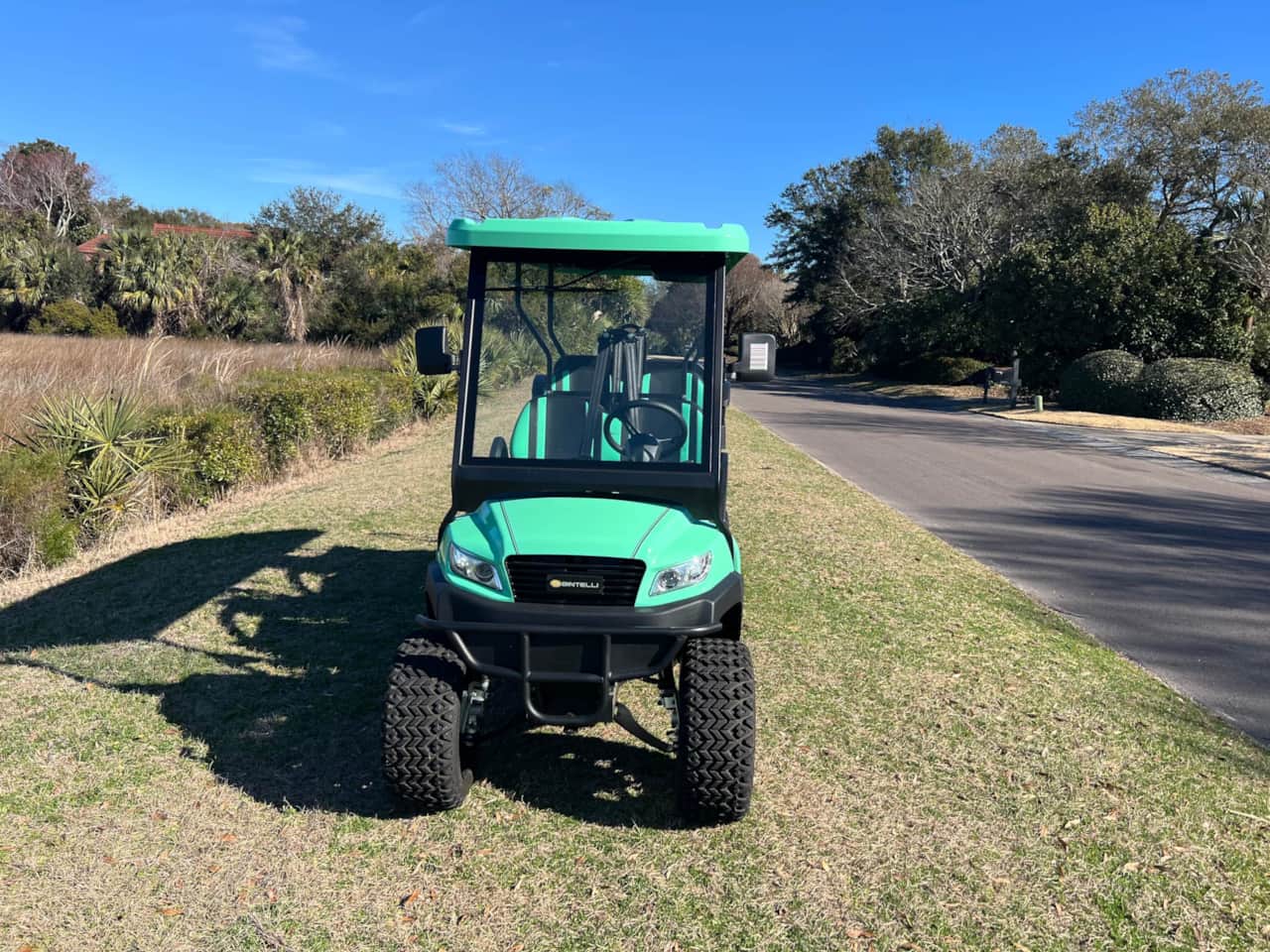 A green golf cart parked on the side of a road.