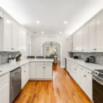 A kitchen with white cabinets and wood floors.