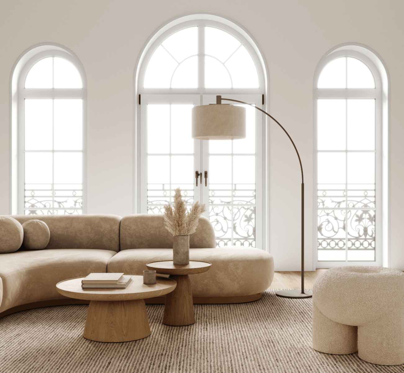 Minimalist living room with a beige sectional sofa, two wooden coffee tables, decor items, a curved floor lamp, and arched windows with white frames and decorative railings.